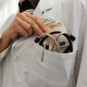Ein Mann im Arztkittel steckt sich ein Bündel Geldscheine in die Tasche