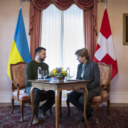 Viola Amherd, Bundespräsidentin der Schweiz, spricht an einem Holztisch mit Wolodymyr Selenskyj, Präsident der Ukraine - beide haben ihre jeweiligen Landesfahnen im Rücken und sitzen vor einem Fenster.