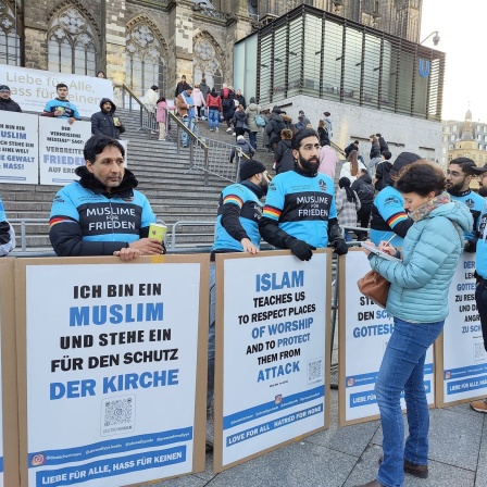 Mitglieder der Ahmadiyya-Gemeinde stehen mit Transparenten vor dem Kölner Dom