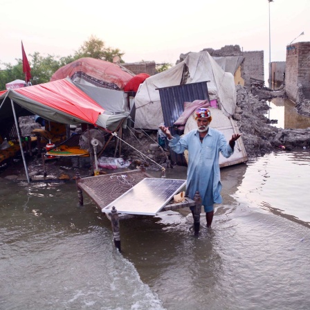 Ein Mann steht in den Fluten in Pakistan vor zerstörten Häusern.