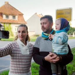 Anne Münch mit Mann und Kind vor dem Ortseingangsschild von Lenzen in der rbb-Doku.