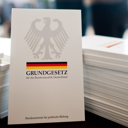 Ein Grundgesetzbuch steht vor einem Stapel von Grundgesetzbüchern