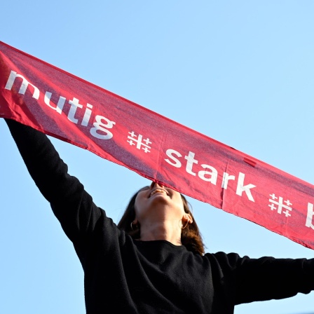 Eine junge Frau hält einen Schal mit dem Motto des Evangelischen Kirchentags: mutig, stark, beherzt