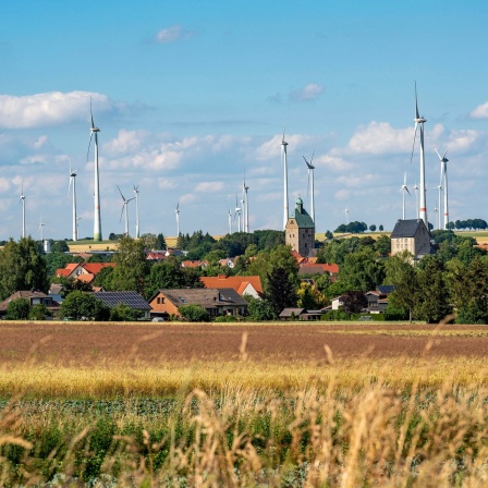 Landschaftsaufnahme einer Ortschaft hinter der ein Windpark aufragt.