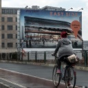 Radfahrer vor groß plakatierter Hausfront in Berlin.