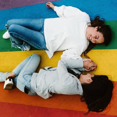 Zwei Frauen liegen auf einer Regenbogenflagge