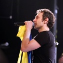 Swjatoslaw Wakartschuk steht auf einer Bühne und hält sowohl ein Mikrofon als auch eine blau-gelbe Flagge in der Hand.