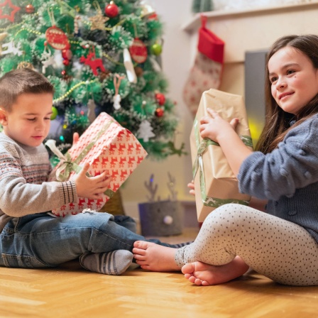 Kinder mit Geschenken vor einem Weihnachtsbaum