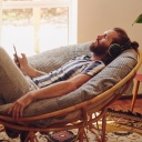 Ein Mann liegt zurückgelehnt in einem Sessel und meditiert. Er trägt Kopfhörer und hält ein Smartphone in der Hand.