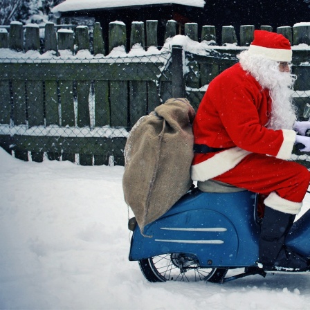 Ein Weihnachtsmann fährt auf einer Vespa durch den Schnee.