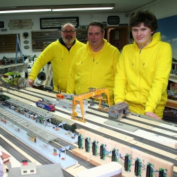 Drei Menschen stehen vor einer Miniatureisenbahn-Anlage
