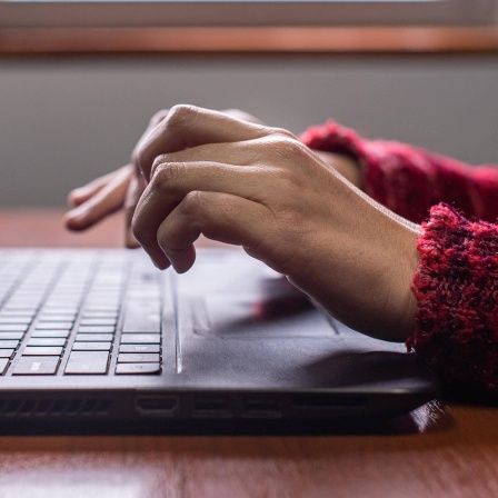 Seitenansicht einer weiblichen Hand, die auf einer Laptop-Tastatur in der Nähe des Fensters tippt