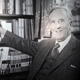 Porträt des Schriftstellers J.R.R. Tolkien: er steht lächelnd vor einem großen Bücherregal