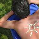 Ein junger Mann ha mit Sonnencreme eine Sonne auf den Rücken gemalt.