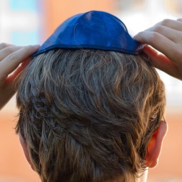 Ein Junge setzt sich eine Kippa auf den Kopf.