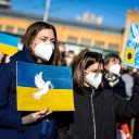 Eine Friedenstaube ist auf dem Plakat einer Demonstrantin auf einer Demonstration gegen den Angriff Russlands auf die Ukraine zu sehen; auf einem weiteren Plakat ist der Schriftzug "peace" zu lesen