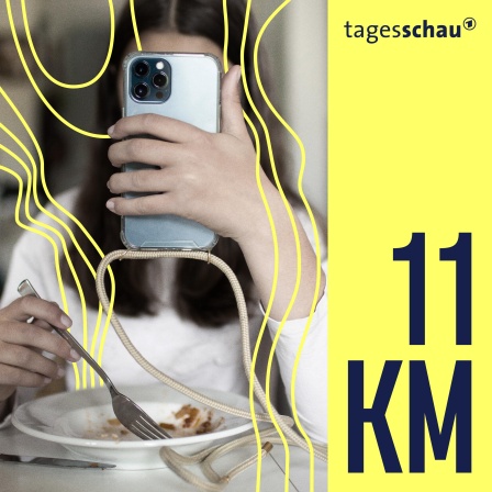 Ein junges Mädchen schaut auf ihren Handybildschirm während sie etwas isst.