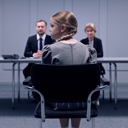 Szene aus dem Film "Quiet Life": Ein blondes Mädchen sitzt auf einem Stuhl vor drei Erwachsenen, die an einem Tisch sitzen