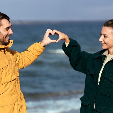 Ein Paar am Strand beschreibt ein Herz mit den Händen.