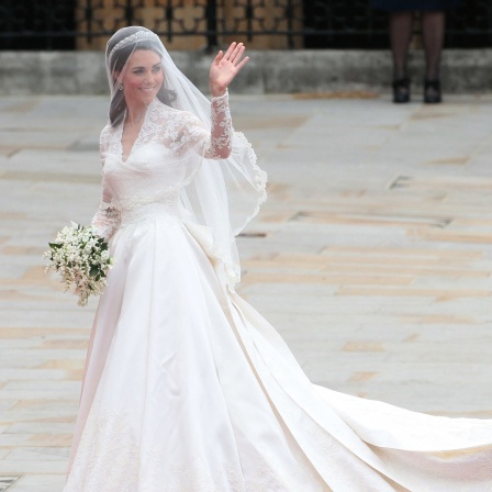 Royale Brautkleider - die Trends im britischen Königshaus: Prinzessin Kate trägt bei ihrer Hochzeit ein weißes Kleid und winkt. Die Schleppe hält ihre Schwester Pippa.