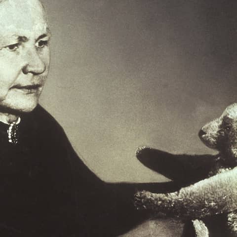 Schwarzweiß-Foto: Margarete Steiff schaut sich einen Teddybären an.