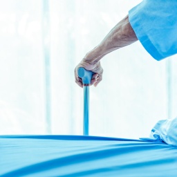 Ein Mensch in blauer Krankenhausbekleidung stützt sich auf einen blauen Gehstock.