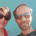 Eva, mit Sonnenbrille und braunem Haar, und Deepak, auch mit Sonnenbrille und braunem Haar, blicken in die Kamera, im Hintergrund Grafiken von Berge und Quallen.