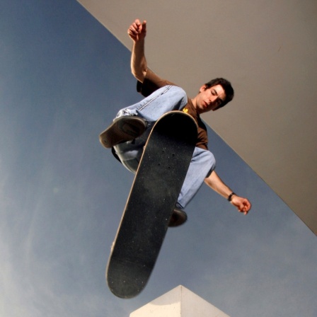 Ein junger Mann springt mit einem Skateboard. 