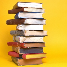Stapel alter Bücher mit Einbänden am linken Bildrand vor einem neutralen, gelben Hintergrund.