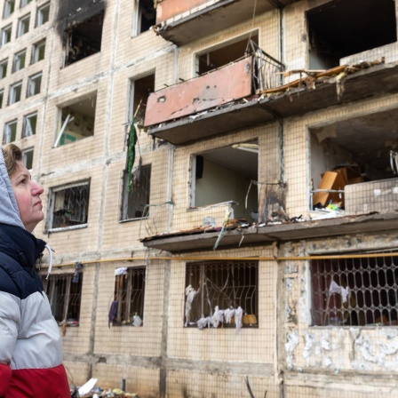 Eine alte Frau steht vor einer Ruine eines Mehrfamilienhauses in der Ukraine