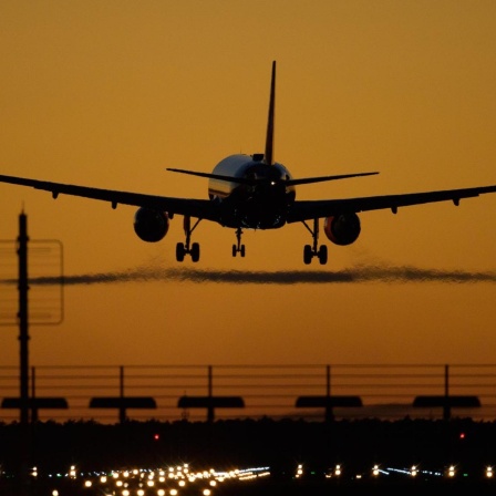 Ein Flugzeug landet auf dem Flughafen Berlin Brandenburg (BER) vor rotem Abendhimmel.