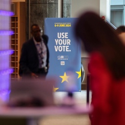 Zwei Menschen im Europäischen Parlament, dahinter ein Plakat mit der Aufschrift "Use Your Vote".