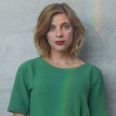 Eine junge Frau steht vor einer grauen Wand und trägt ein grünes T-Shirt.