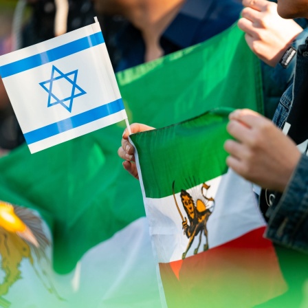 Eine Frau hält eine israelische und eine iranische Fahne während einer Kundgebung auf der Wiese gegenüber des iranischen Konsulats in Hamburg.