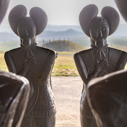 Repliken der Statue des "Keltenfürsten vom Glauberg" - mit Blick auf den großen Grabhügel - stehen beim Museumsgebäude der Keltenwelt am Glauberg.