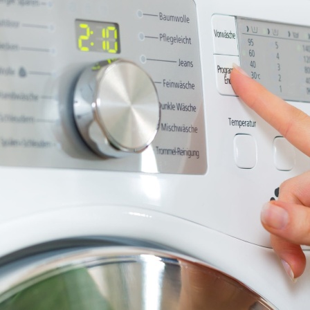 Mann sieht die Hand einer Frau, die die Programmwahltaste einer Waschmaschine drückt.