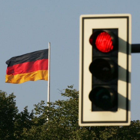 Auf Rot steht die Ampel neben der schwarz-rot-goldenen Fahne der Bundesrepublik Deutschland © picture-alliance/ ZB/ Soeren Stache 