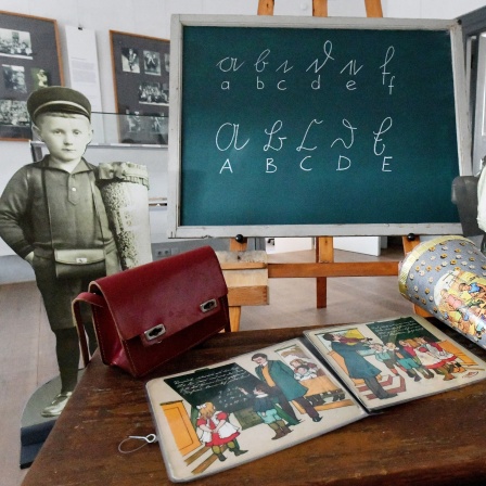 Brottasche, Fibel und Zuckertüte liegen auf einer historischen Schulbank im Museum Viadrina in der Sonderausstellung &#034;Von ABC Schützen und Zuckertüten&#034;: Schulen gab es bereits bei den Sumerern, also im 3. bis 4. Jahrtausend vor Christus.