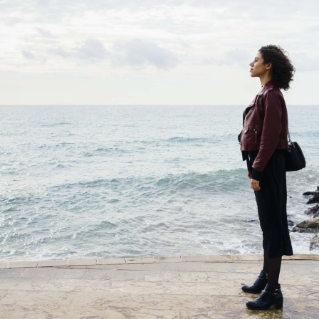 Frau steht am Meer und Blickt in die Ferne