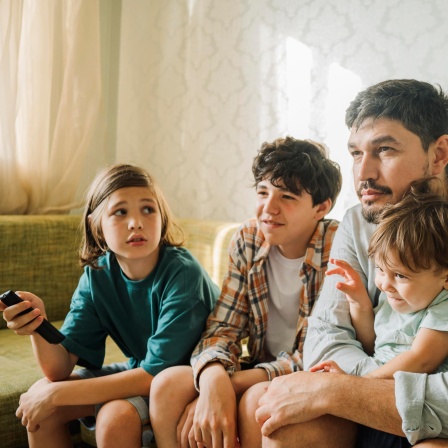 Ein Vater guckt mit seinen drei Kindern fern.