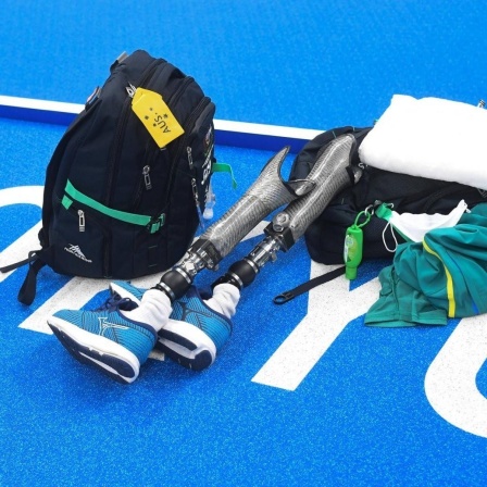 Auf blauem Untergrund mit dem weißen Schriftzug Tokio liegen ein Rucksack, ein Handtuch, Schwimmkleidung und zwei Beinprothesen. 