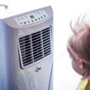 Kind steht vor mobiler Klimaanlage