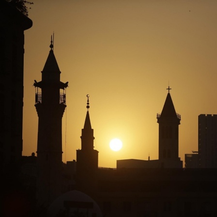 Die Dächer von Kirchen und Moscheen heben sich als Silhouetten vor einem Sonnenuntergang ab.