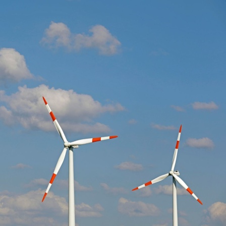 Zwei Windräder stehen vor blauem Himmel.