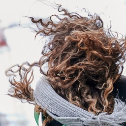 Eine Frau mit Schal um den Hals und im Wind wehenden Haaren bewegt sich im Freien