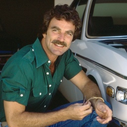 Der Schauspieler Tom Selleck kniet an einem Fahrzeug