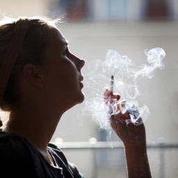 Eine Frau im Seitenprofil sitzt am Fenster und raucht