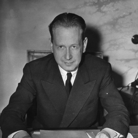 Dag Hammarskjöld sitzt an einem Schreibtisch und schaut in die Kamera.