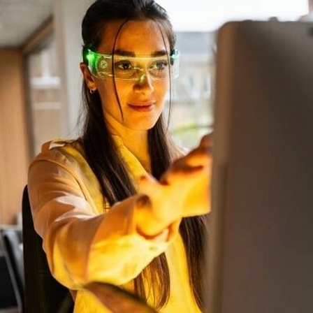 Eine Frau hat eine Smartbrille auf und sitzt vor einem PC.