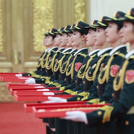 Abgebildet sind mehrere chinesische Frauen in Uniformen, die rote Schachteln in ihren Händen halten.